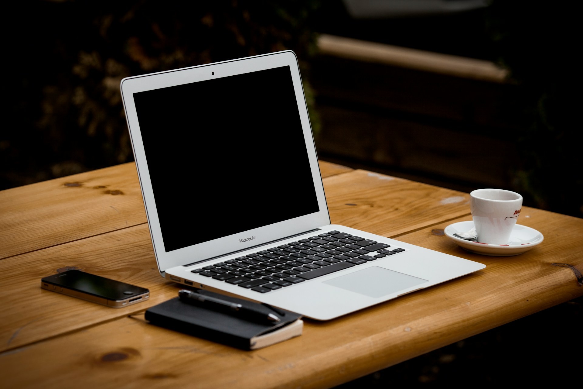 A laptop, cup of coffee, mobile phone and notepad on a wooden table.